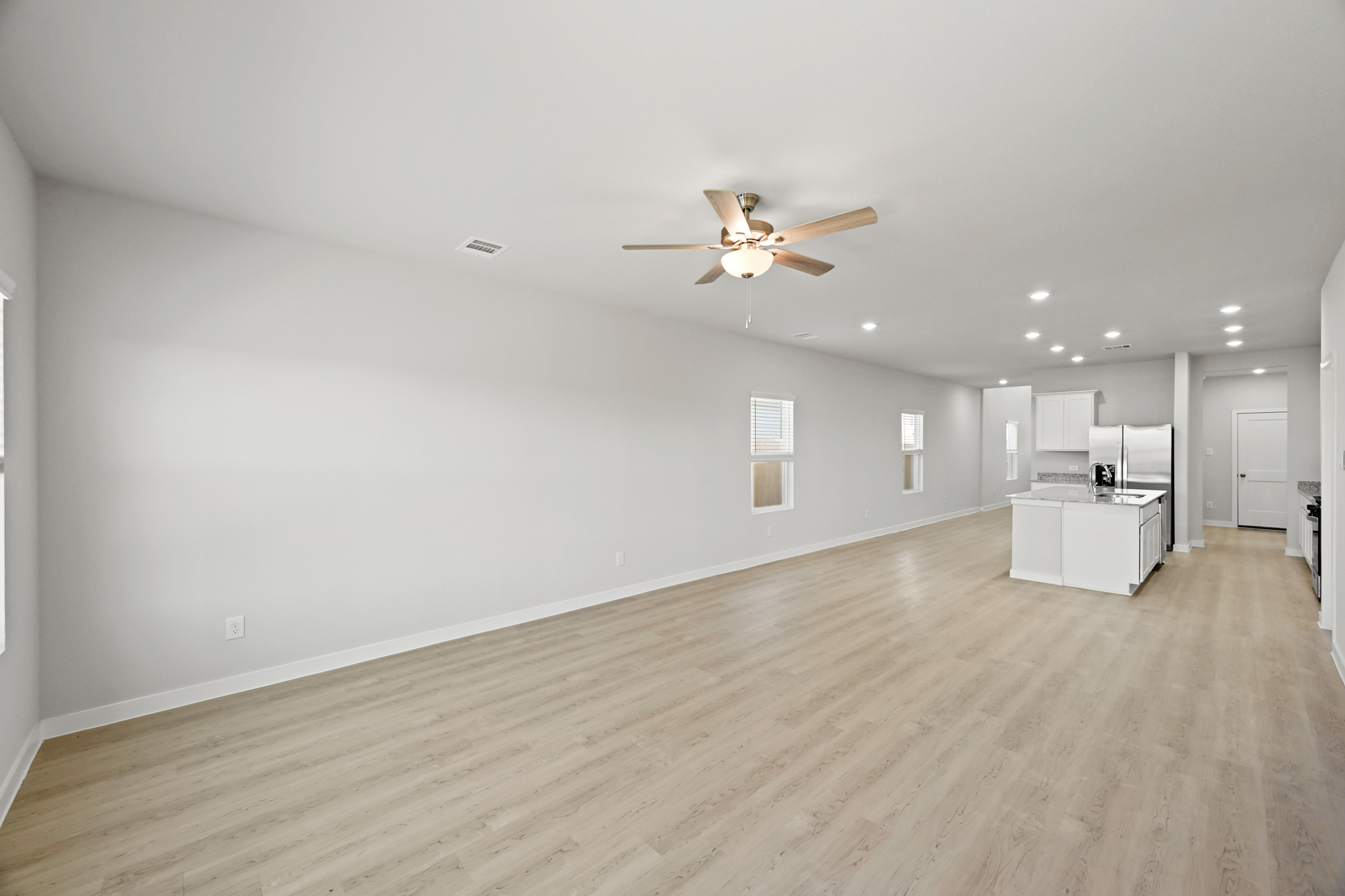 A large empty room with a ceiling fan and a wood floor.